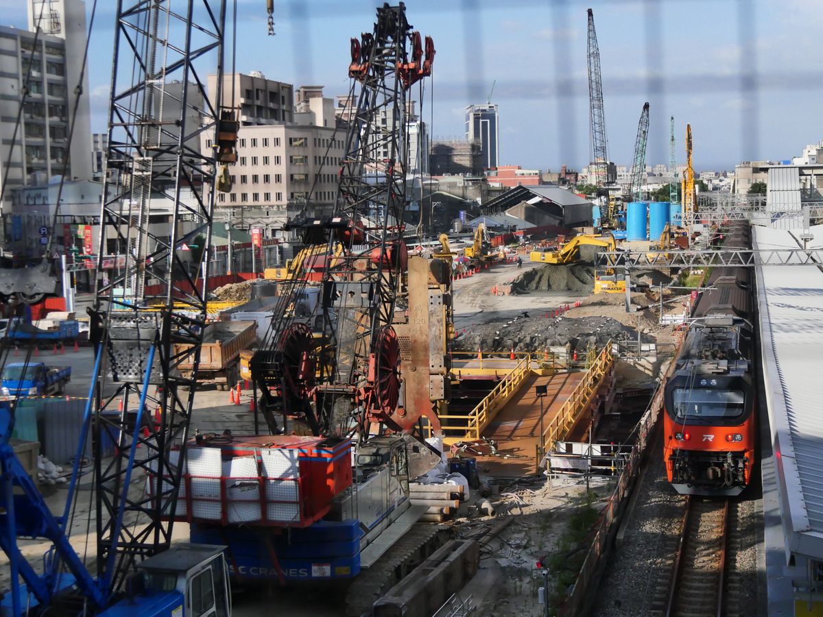 Cranes and heavy equipment at a railway construction site beside a passing train