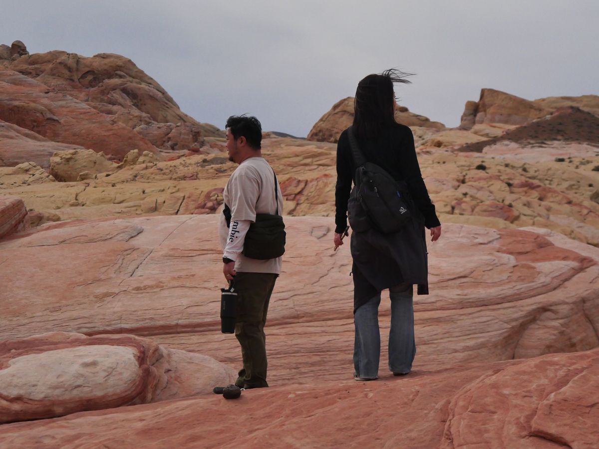 Two people walking across banded red and cream sandstone in the Nevada desert
