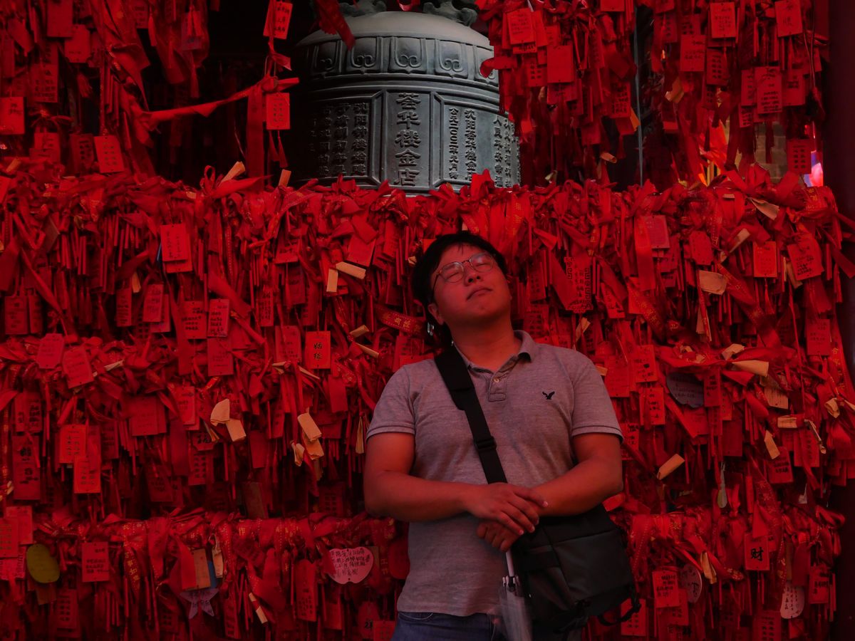 A wall of red wish ribbons and prayer tablets surrounding a bronze bell